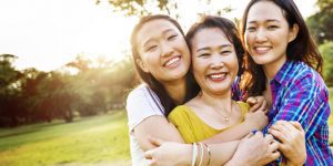 Two daughters hugging their mother and smiling at the camera with trees in the background for women and mothers IGNITE Peak Performance coaching service