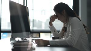 Photo of woman sitting at a desk with her head down in frustration