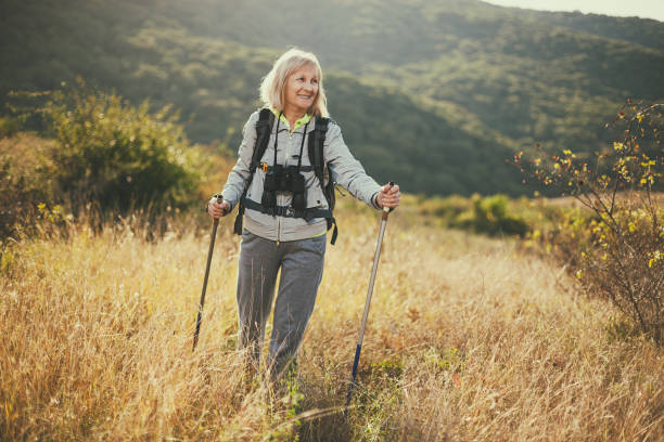 Image of older woman with short grey hair hiking through field of gold wheat with hiking poles