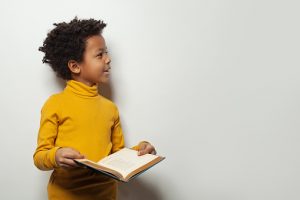 Image of child holding a book and looking up to the side of the image to indicate giftedness