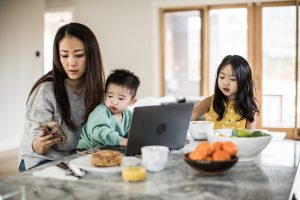 Mom working from kitchen with two children around