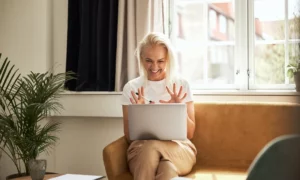 Woman sitting on sofa waving at computer screen