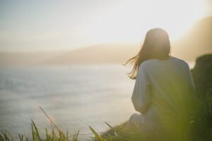 Image of woman sitting on a cliff, overlooking a calm sea