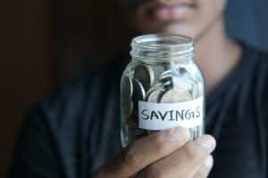 Girl holding a mason jar of 'Savings' up to camera