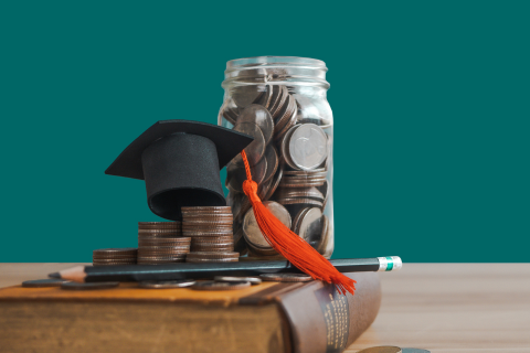 Image of college savings coins in a jar with a graduation cap and gown on a book
