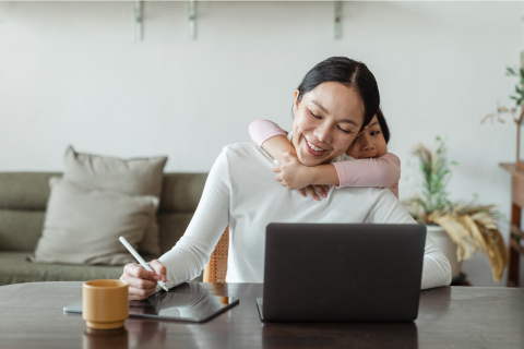 Image of mom working from home with child hugging her